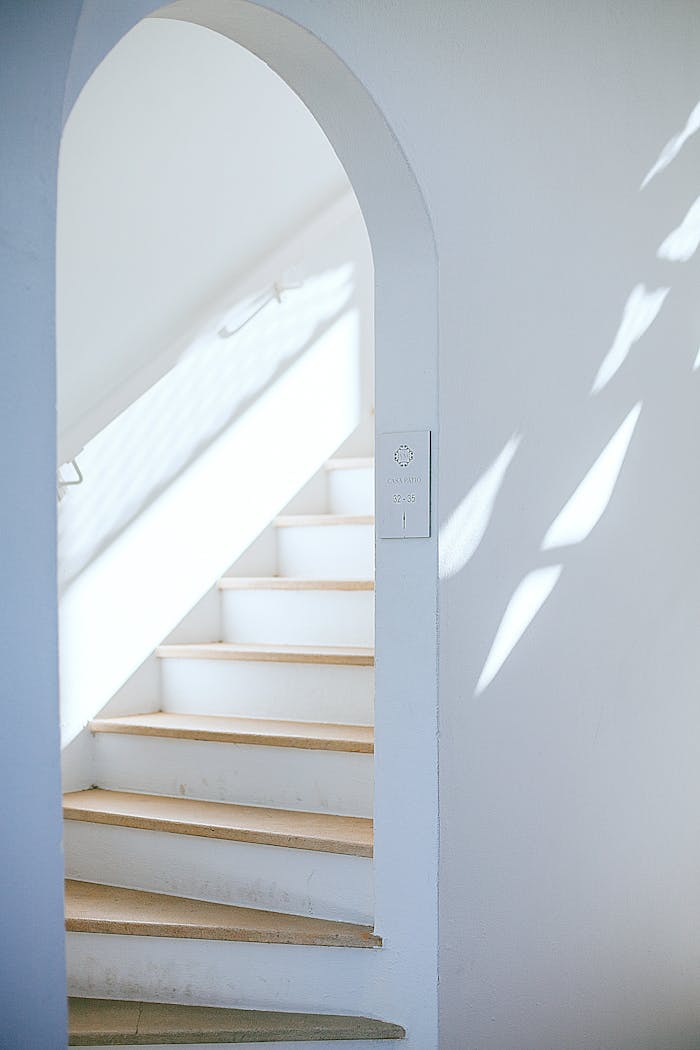 services-02 Bright minimalist interior featuring a white staircase with an arch and natural light casting shadows.